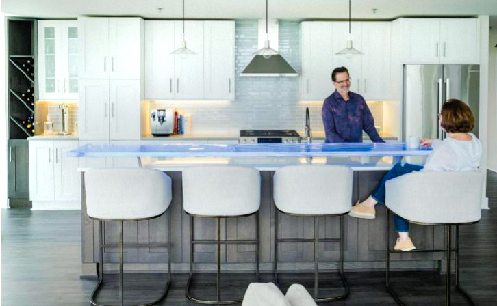 Dr. Don and Kim Toothman at their custom LED-illuminated kiln-formed glass high bar top by Downing Designs — floating above a white glass island countertop, Greenbridge Condominiums, Chapel Hill, North Carolina — published in Chapel Hill Magazine, photography by Cornell Watson