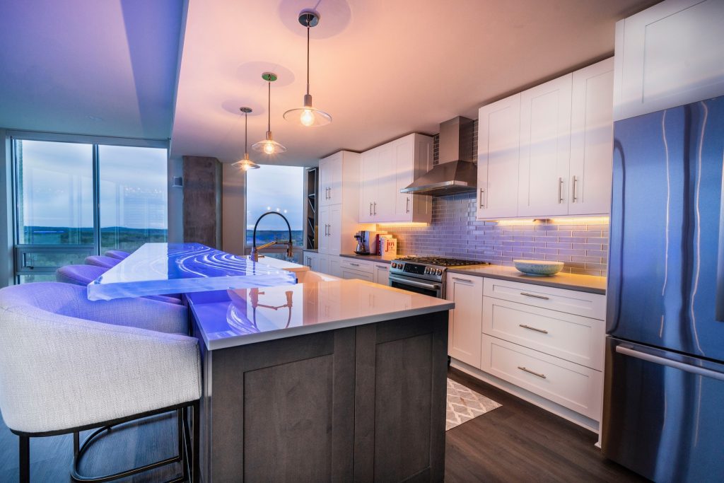 End view of custom kiln-formed glass high bar top by Downing Designs glowing deep blue — Ambiance Machine RGB LED illumination, 126 inches long by 1.5 inches thick, Greenbridge Condominiums, Chapel Hill, North Carolina