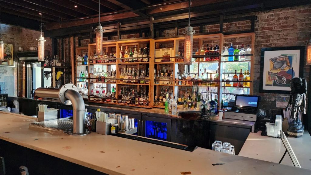 Full-width view of custom concrete bar top at Ulele Restaurant Tampa — artifact-infused surface by Downing Designs, exposed timber beam ceiling, blown glass pendant lighting, Columbia Restaurant Group