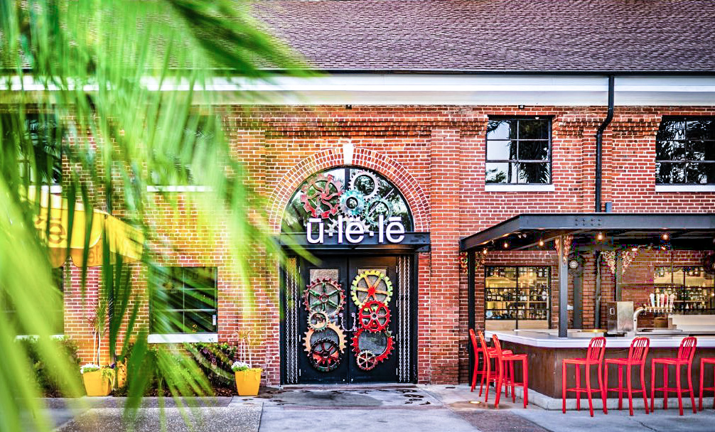 Ulele Restaurant Tampa Heights — custom white glass outdoor bar top by Downing Designs visible at right, iconic gear-work entry doors, historic brick facade, Columbia Restaurant Group
