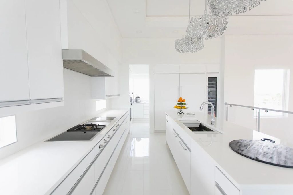 White glass kitchen countertop in a long galley run beneath handleless white cabinetry
